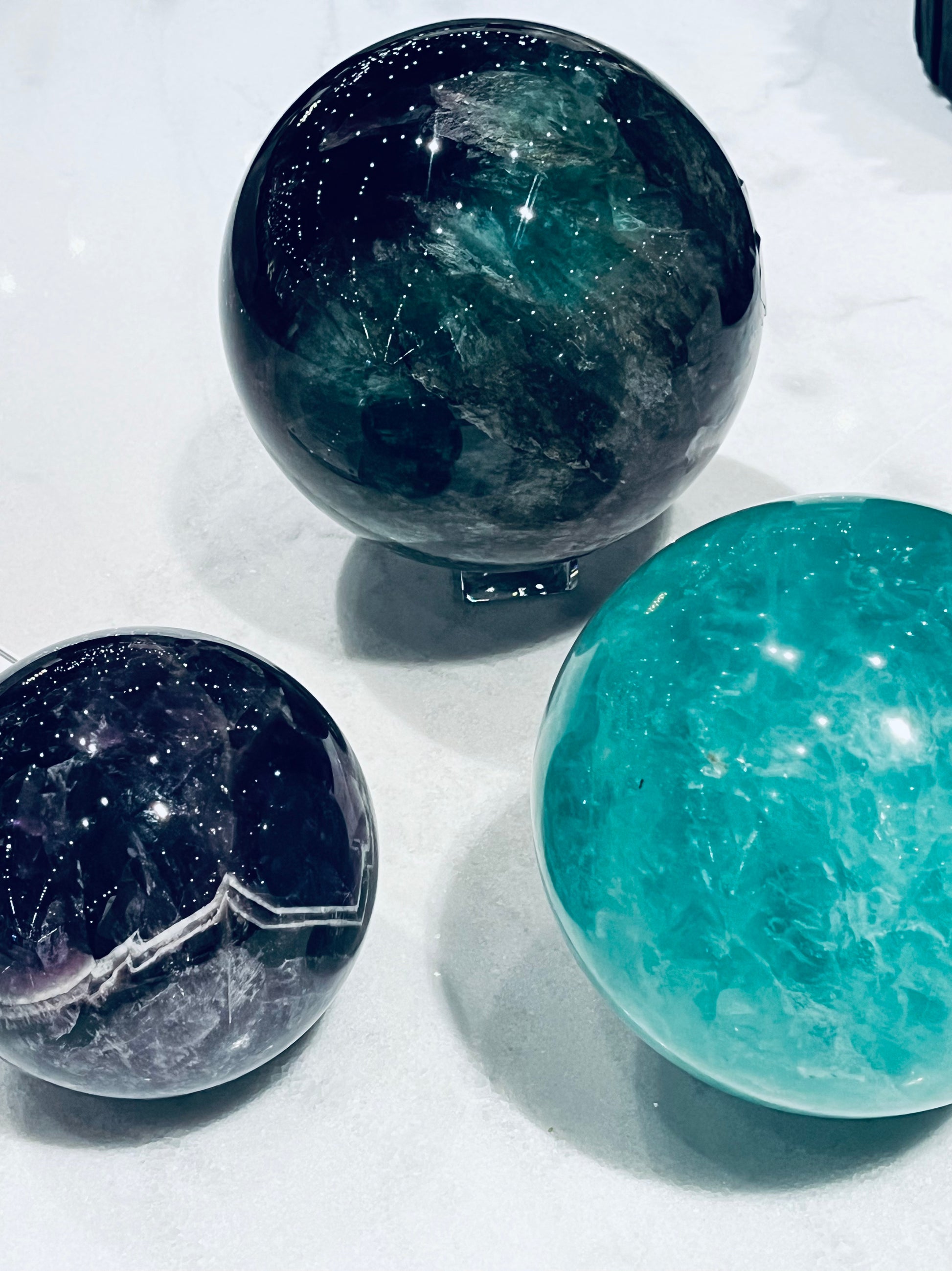 Three crystal spheres, rainbow fluorite, green fluorite and chevron amethyst, on a white surface