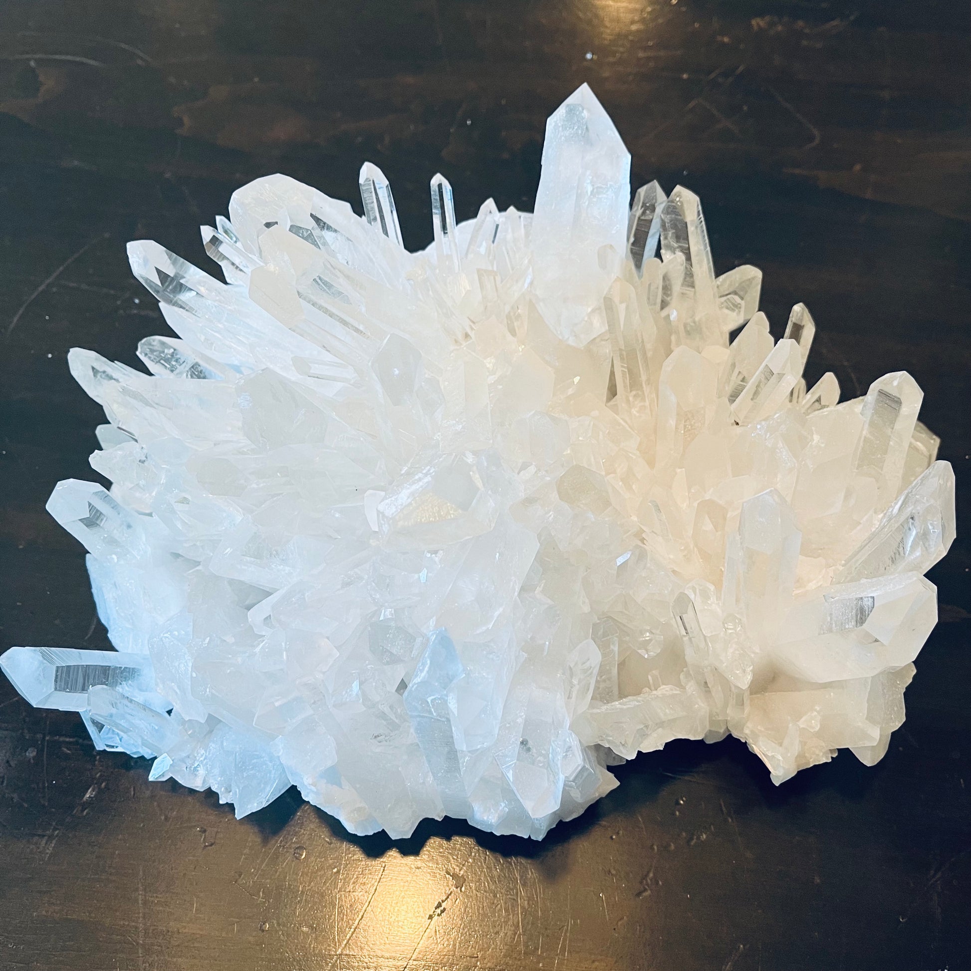A cluster of clear, rough Arkansas quartz crystals with a variety of shapes and sizes, displayed on a dark surface.