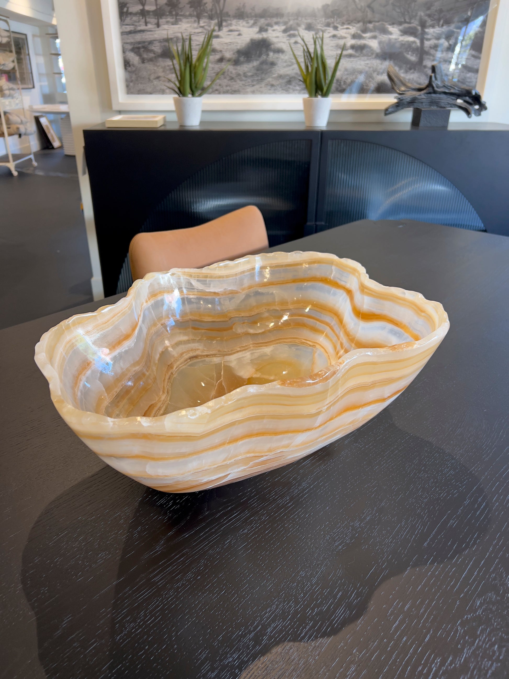 Natural hand carved onyx statement bowl with brown and amber stripes on wood surface and sofa in distance.