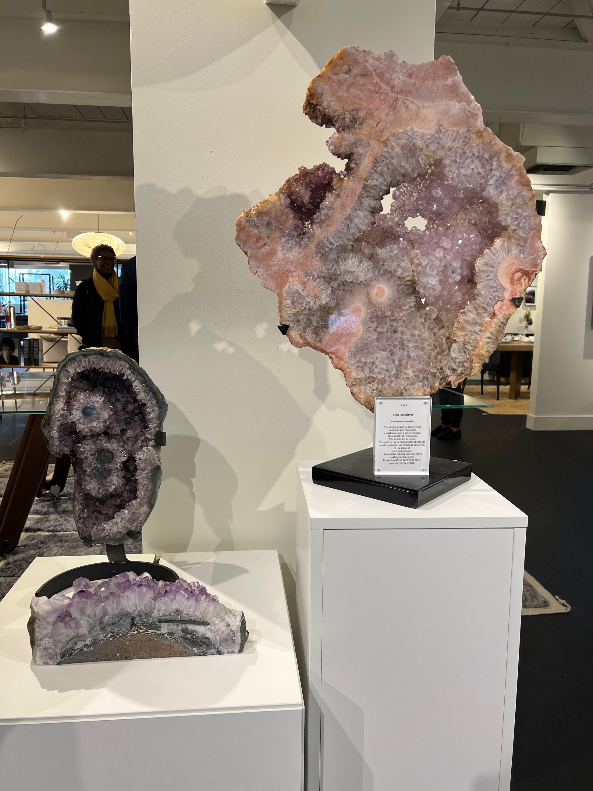 Pink amethyst slab on stand next to 2 amethysts on stand set atop white pedestals