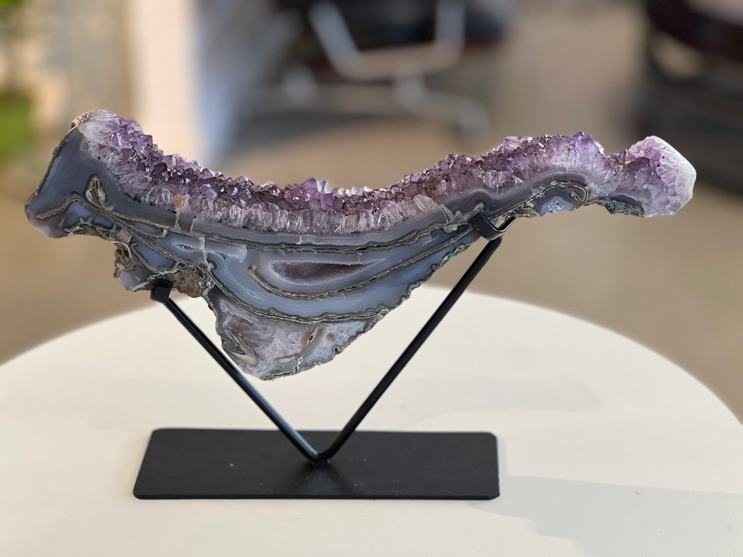 An Amethyst Druzy wave displayed on a stand, showcasing its purple and translucent crystal patterns.
