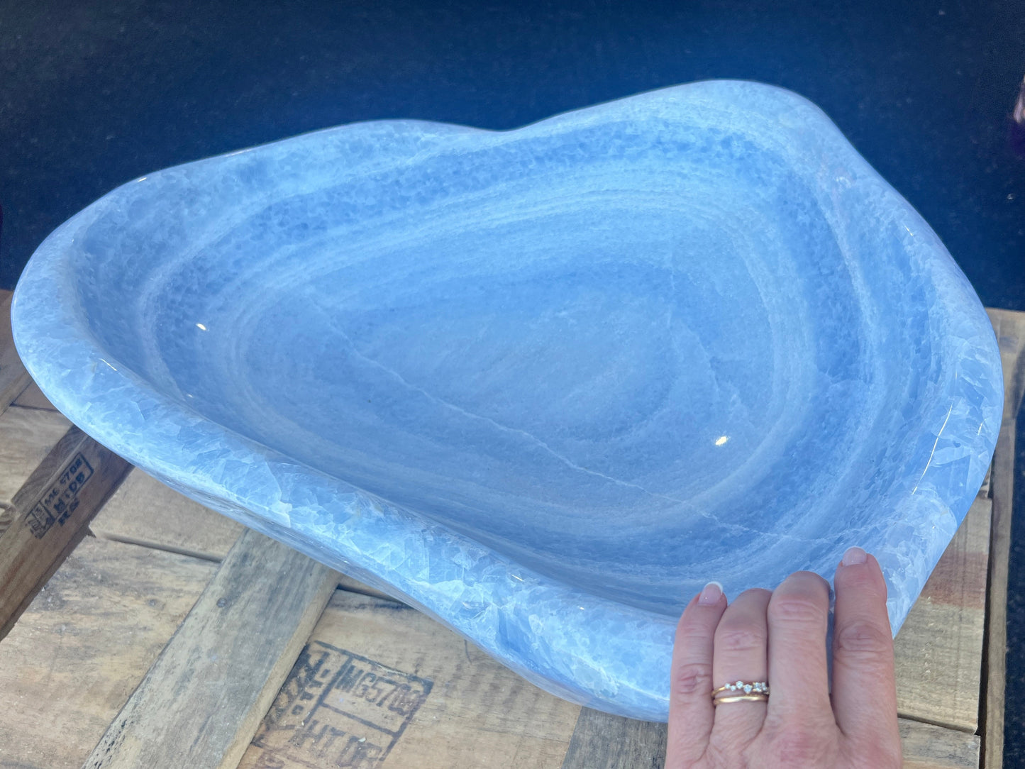 Blue calcite bowl on a wooden surface with a person's hand holding it.