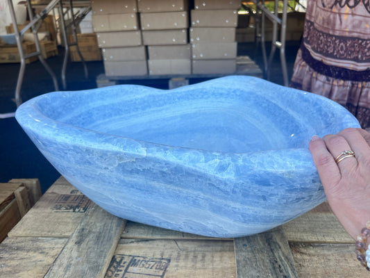 Blue stone bowl held by a person on a wooden pallet with stacked boxes in the background