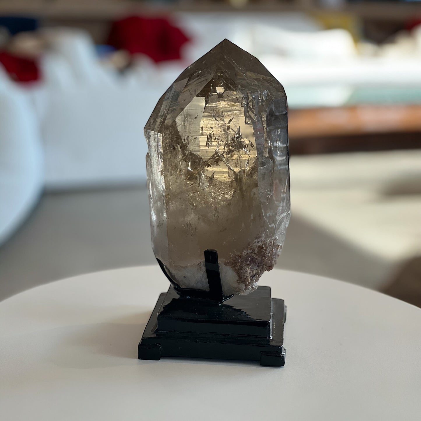 Large golden citrine crystal tower with natural inclusions, displayed on a black metal stand. Styled on white table top in darkened living room
