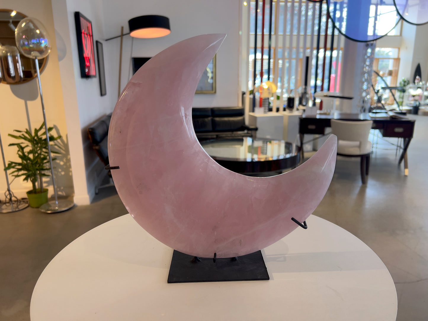 large pink quartz moon in black stand on white table in living room setting