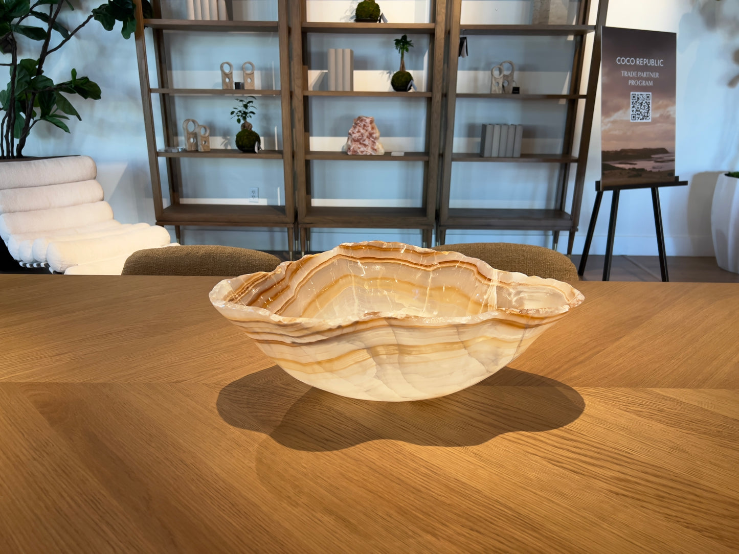 Large flower shaped Onyx Bowl with bands of amber and brown on wooden table with bookshelf in background