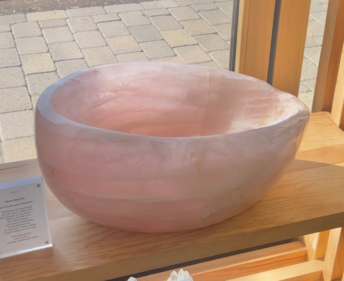 hand carved rose quartz bowl on light wood shelf in a window