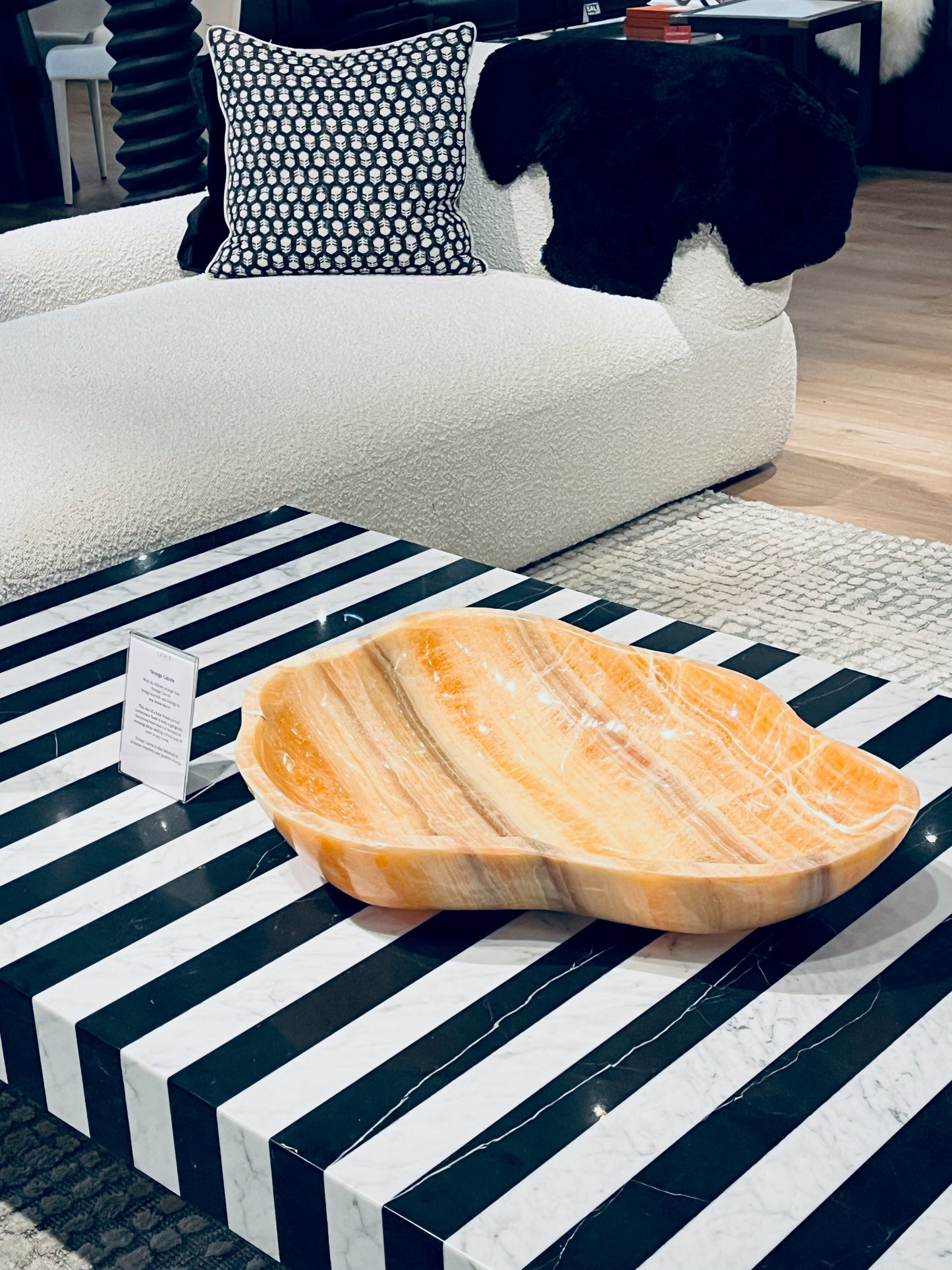 Lg orange calcite bowl angle on black and white coffee table with white sofa in background