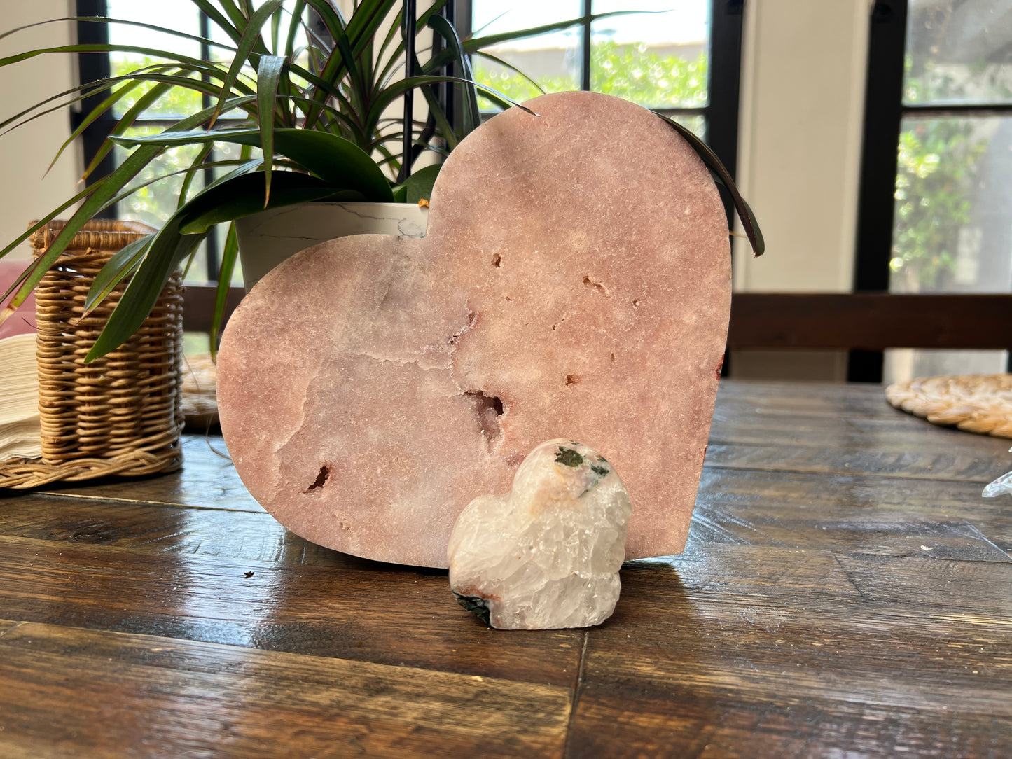 Polished Pink Amethyst heart crystal in soft blush tones, displayed as a decorative stone sculpture for modern home décor with a wicker basket and plant in the background