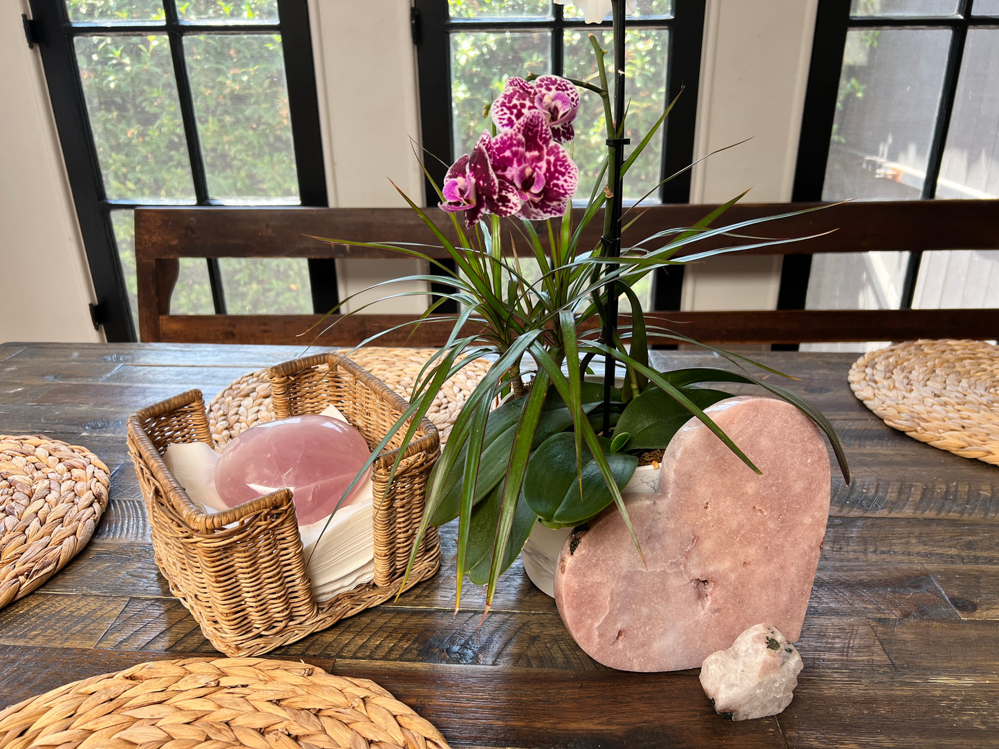 Pink Amethyst Heart shaped crystal on a wooden surface with a wicker basket and plant in the background