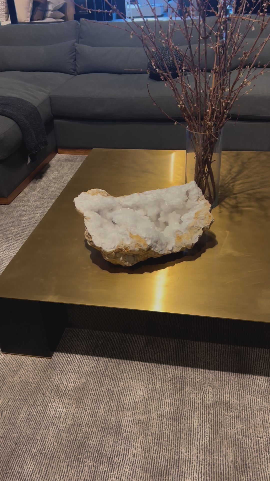 video of xl white geode quartz  displayed on square brass coffee table near grey sofa
