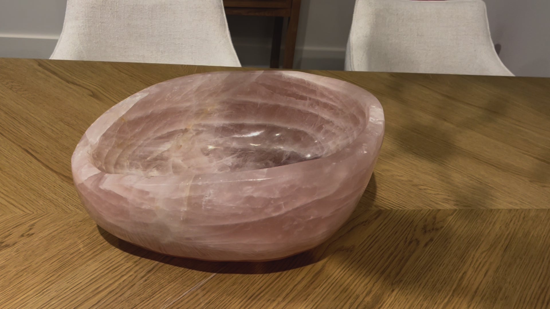 video of a gorgeous xl rose quartz hand carved bowl on wood table in front of white chairs