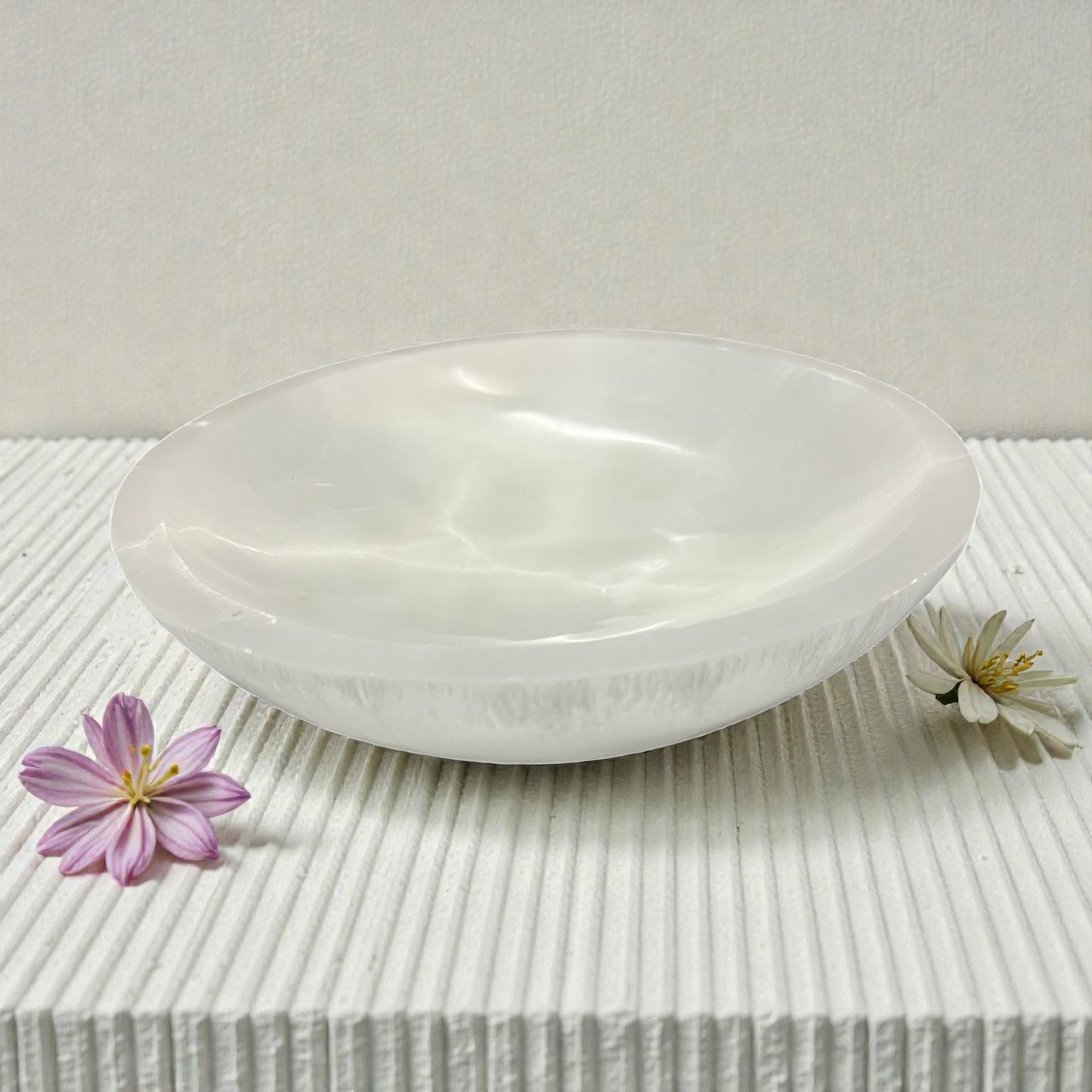 White selenite bowl on a textured surface with flowers