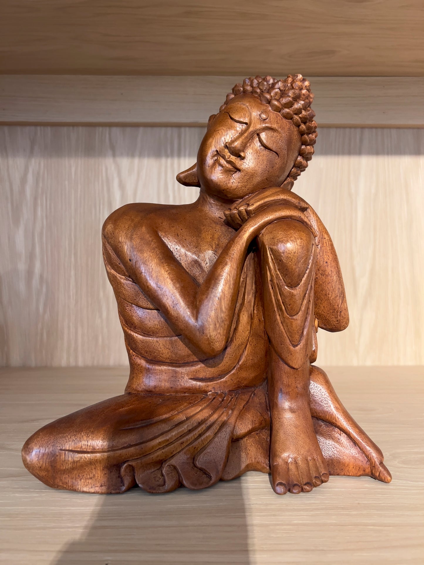A wooden sculpture of Buddha in a meditation pose, with a smooth finish and a brown color tone.