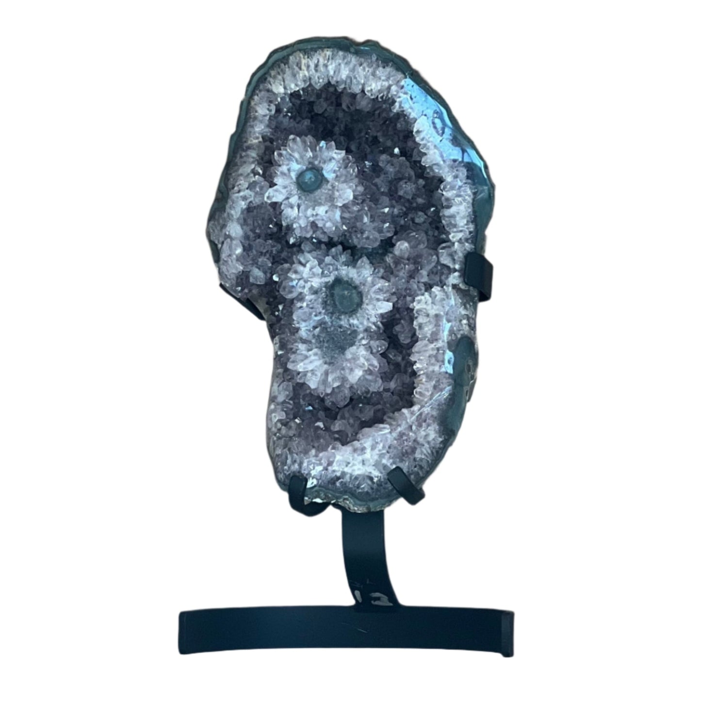 Brazilian amethyst geode featuring rare stalactite flower formations with green centers. Displayed upright on a black metal stand against wood backdrop.