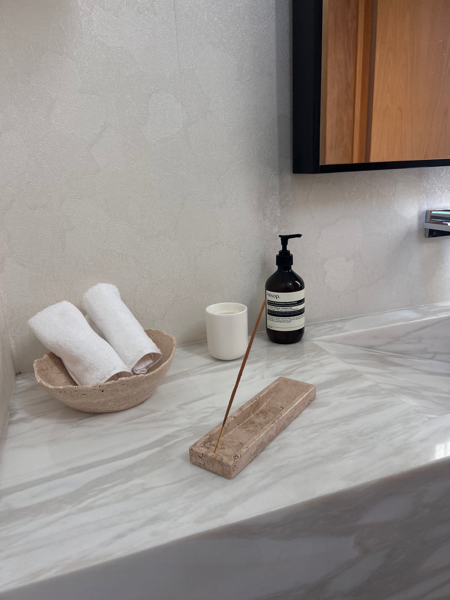 Bathroom counter with rolled towels in a stone bowl, a soap bottle, and an incense stick holder.
