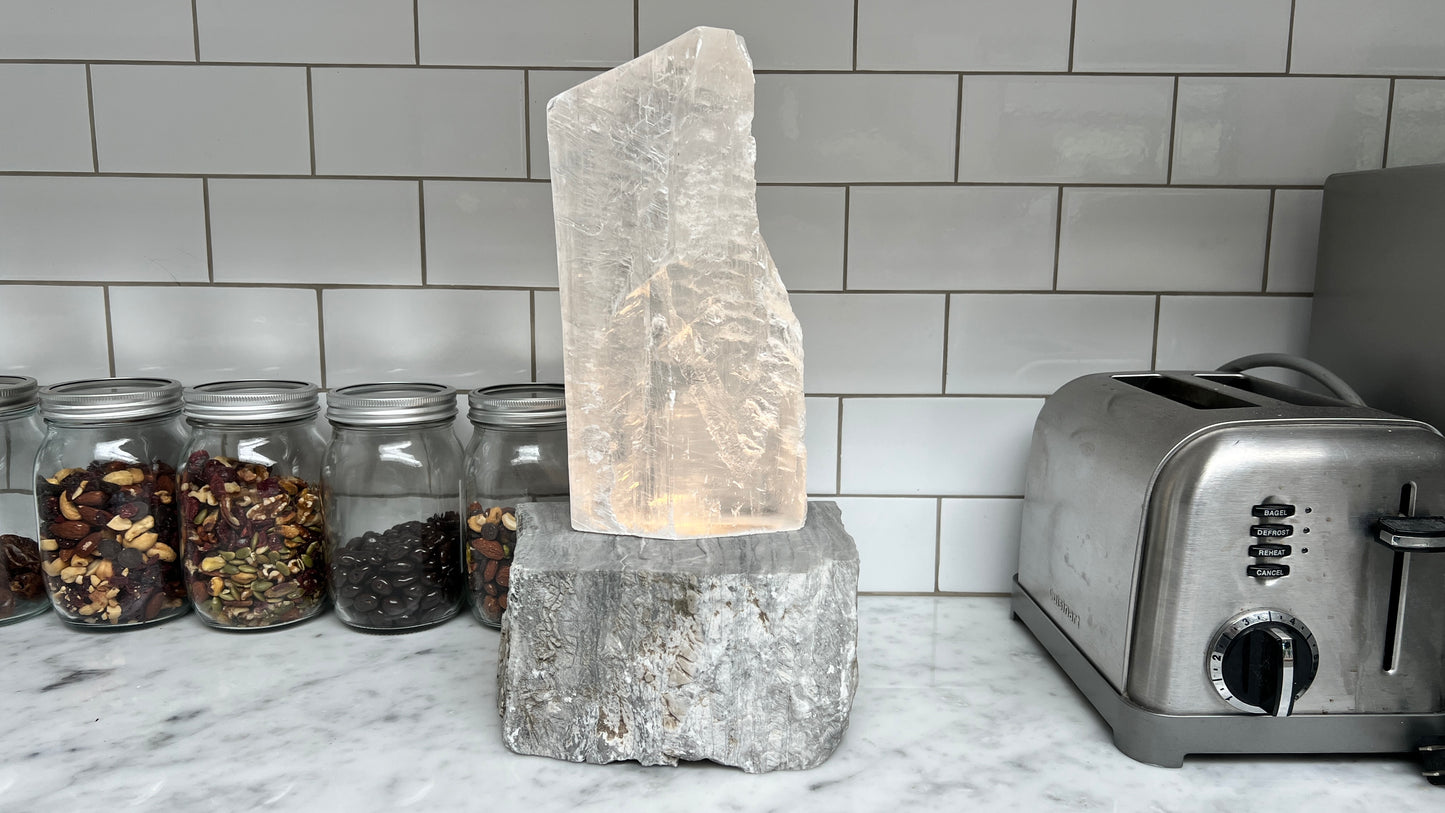 Luminous stone and selenite crystal lamp on a kitchen counter with jars and a toaster in the background.