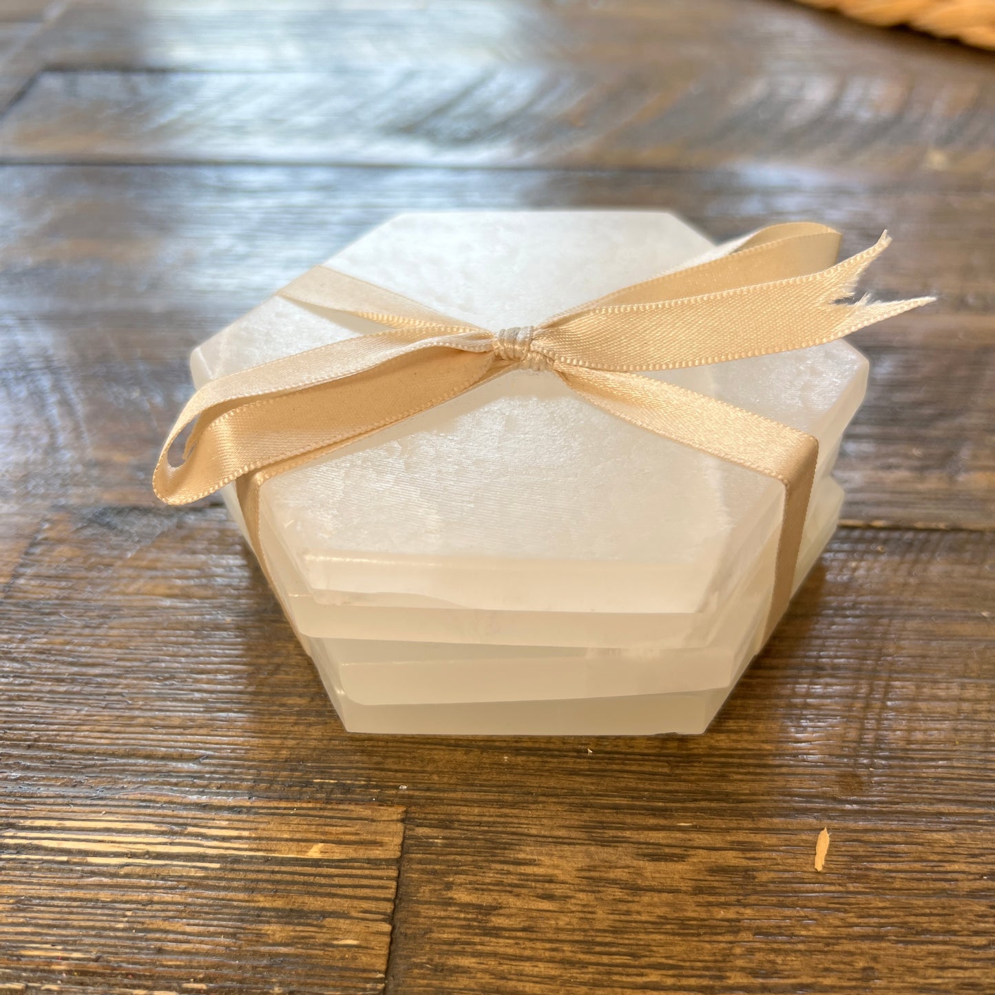 A set of white aragonite stone hexagonal coasters tied with a beige ribbon on a wooden surface