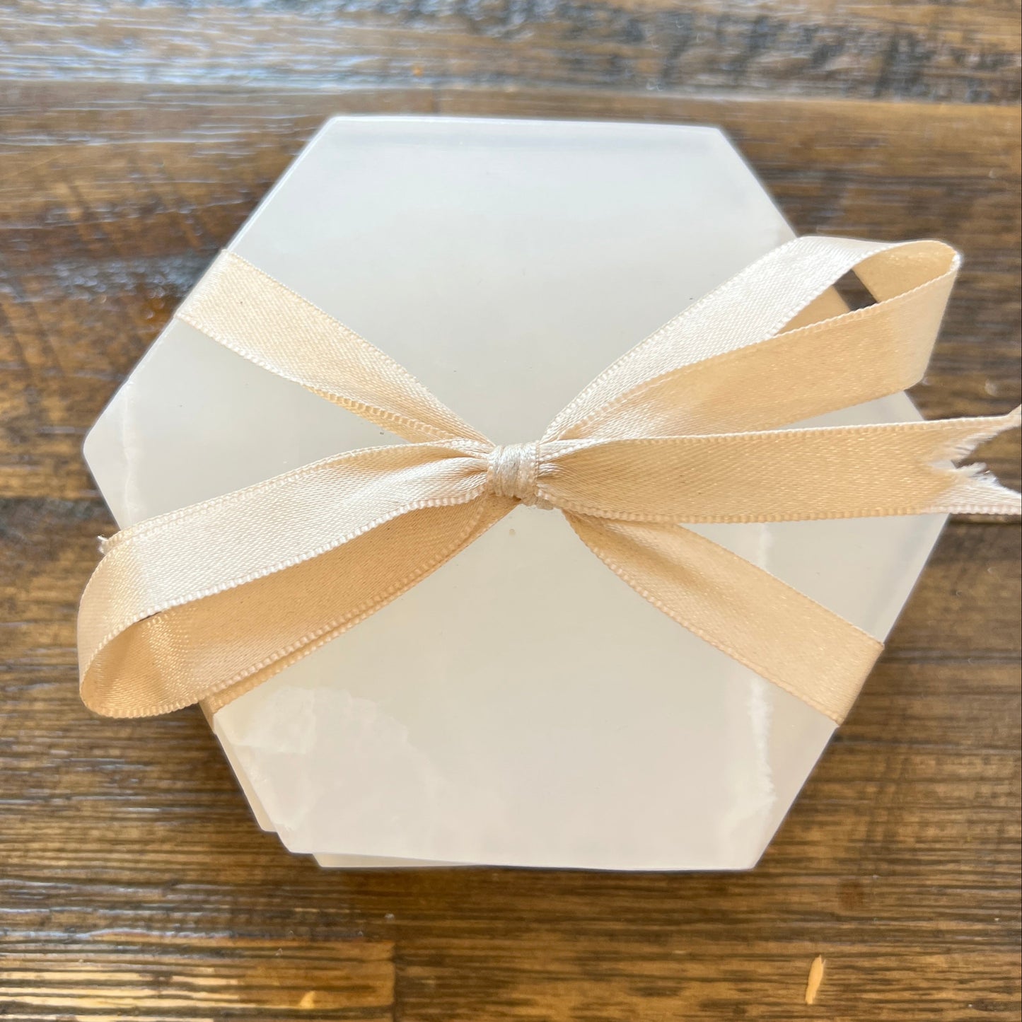 Hexagonal white coasters stack from above with a beige ribbon on a wooden surface