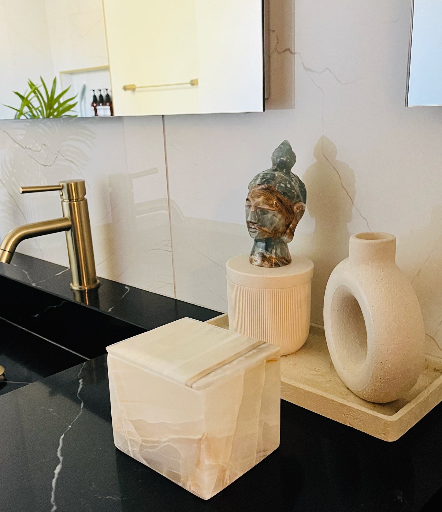 Bathroom counter with black countertop, gold faucet, and decorative items.