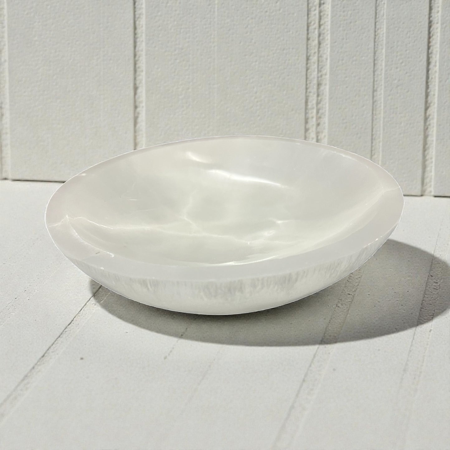 Polished white selenite bowl on a white wooden surface with a white paneled background