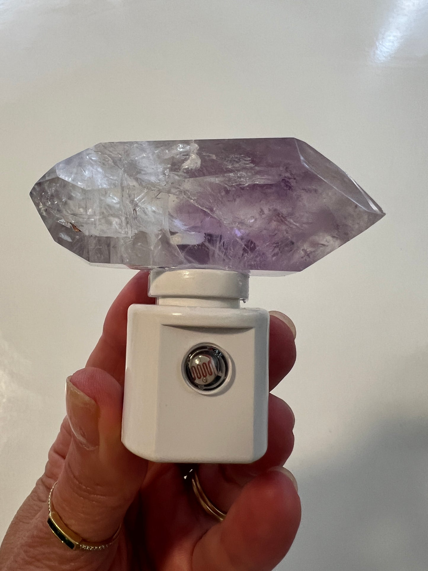Crystal amethyst night light with white base held by a hand with a blurred background
