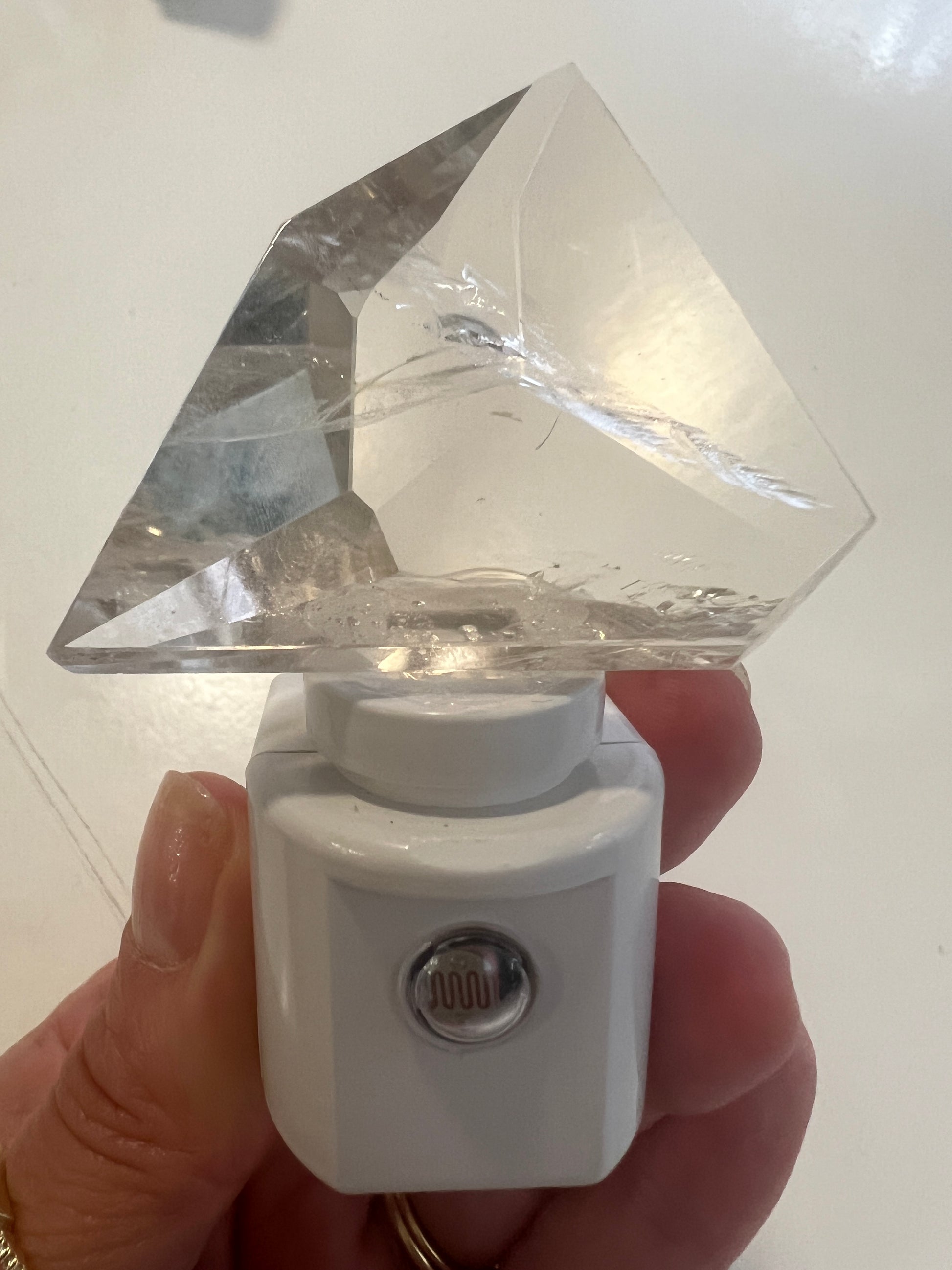 Hand holding a white night light with a clear crystal on a white background