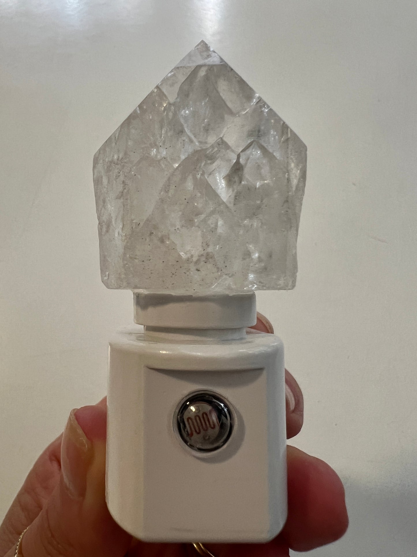 Crystal quartz on a white night light base held by a hand on a light background