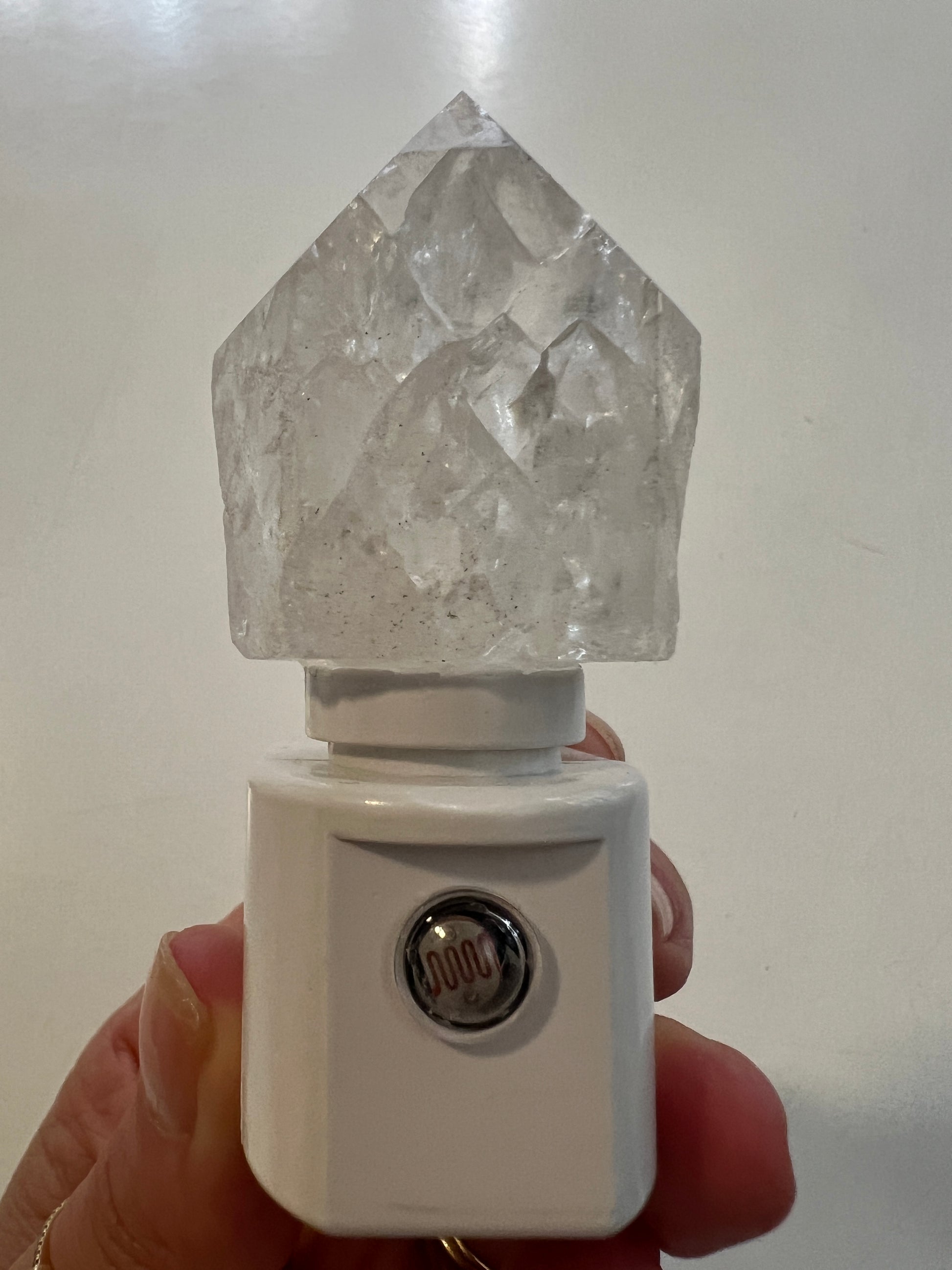 Crystal quartz on a white night light base held by a hand on a light background