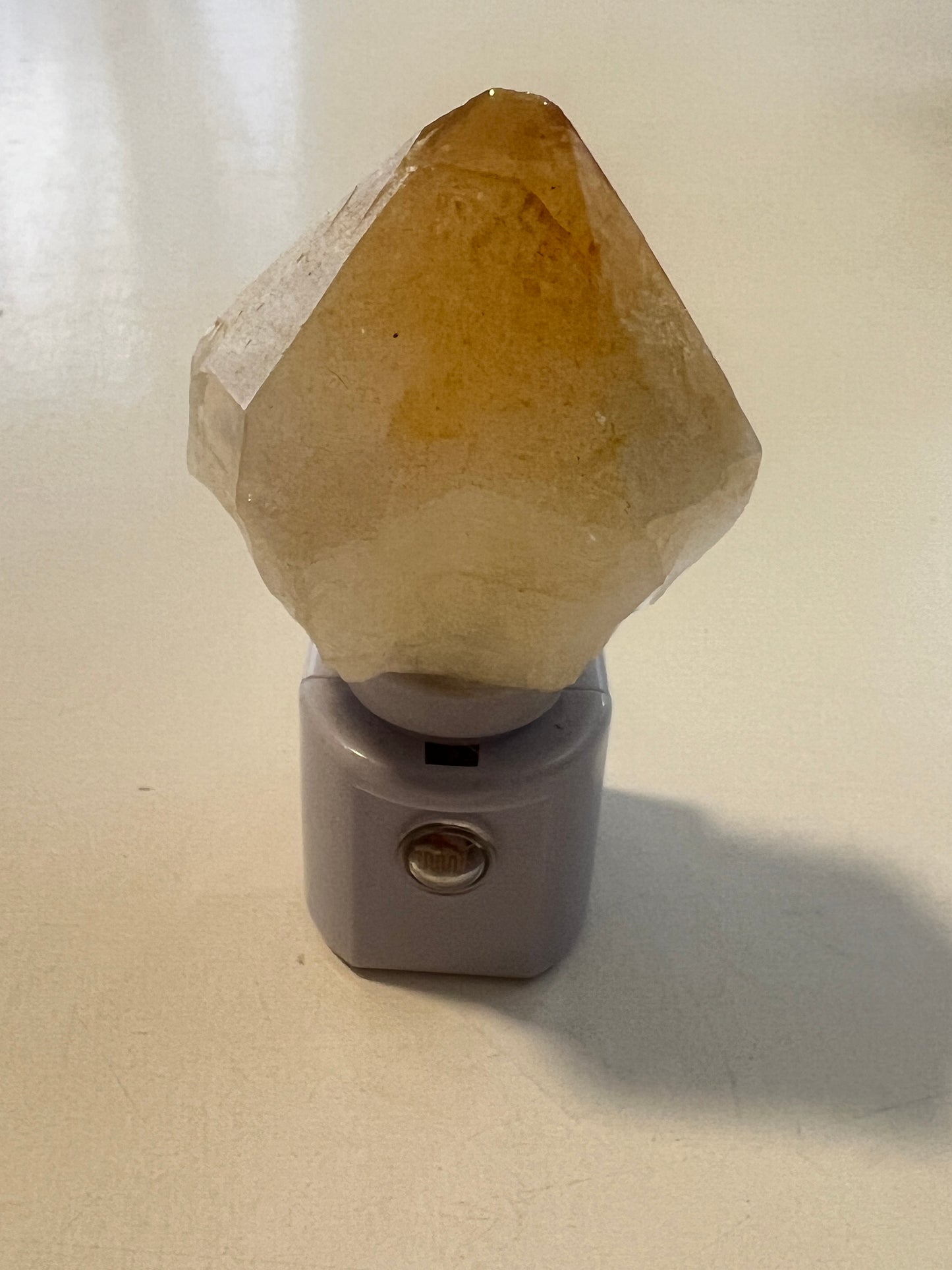 Hexagonal golden healer quartz attached to a gray night light base on a beige surface