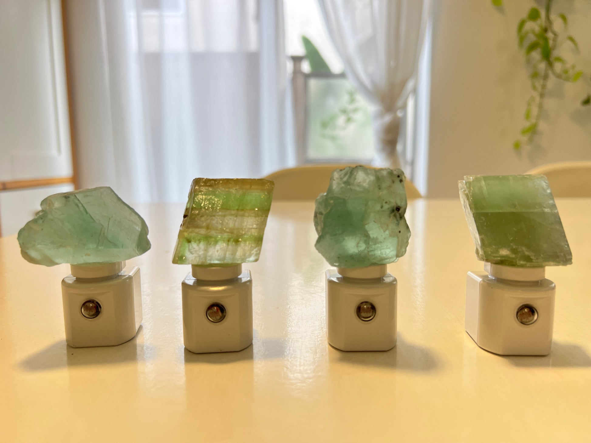 Four green crystal night lights on a white surface with a blurred background