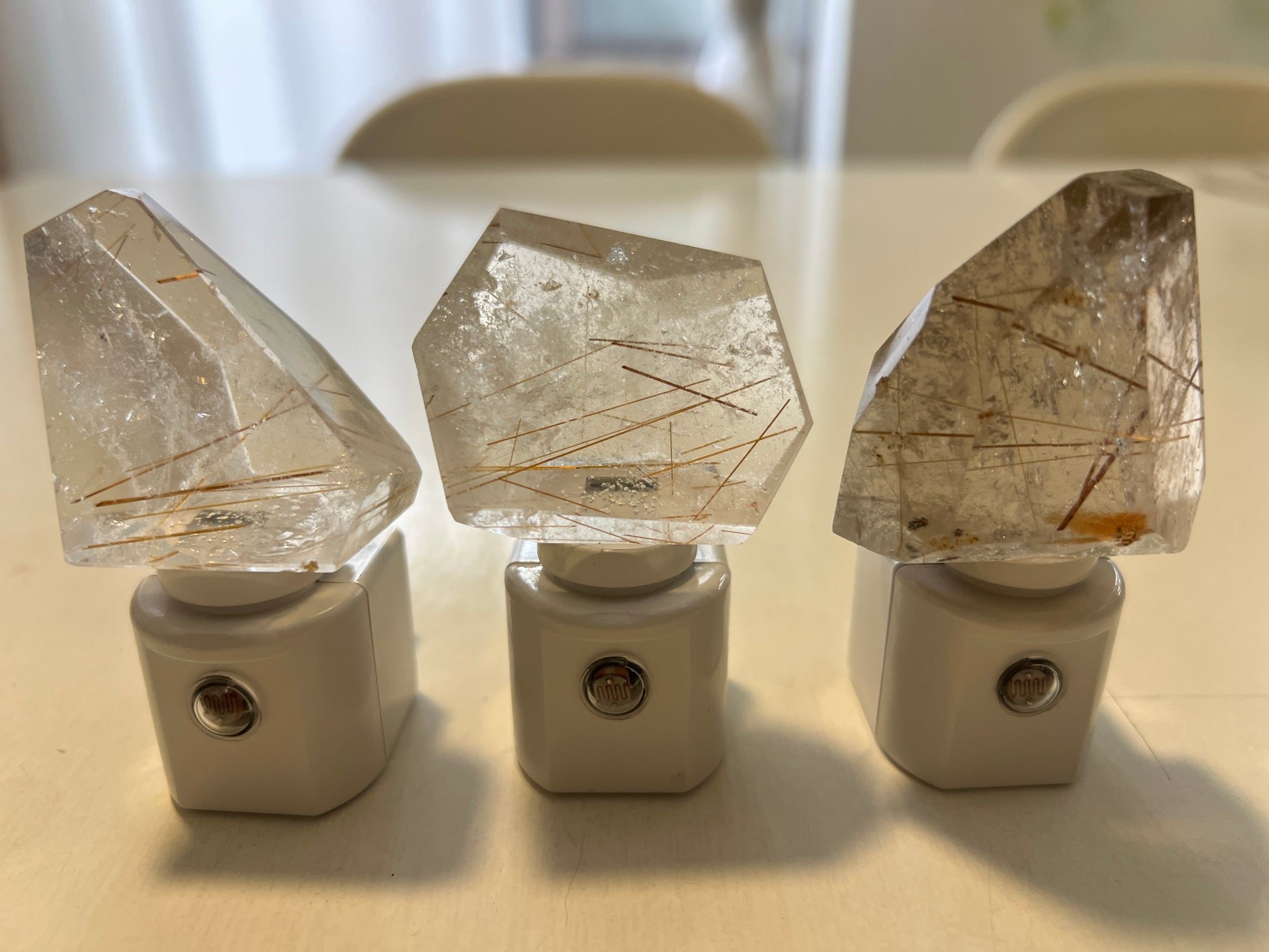 Three crystal night lights with rutilated quartz on a white surface with a blurred background
