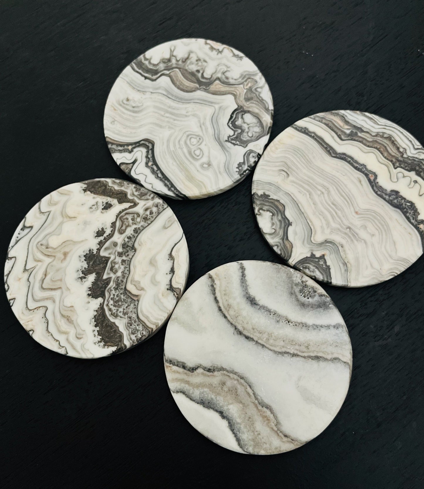 Four round white banded coasters with intricate patterns on a black surface