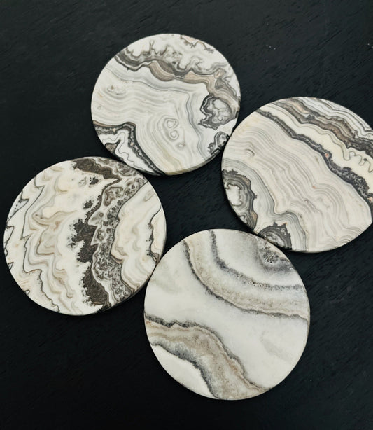 Four round white banded coasters with intricate patterns on a black surface