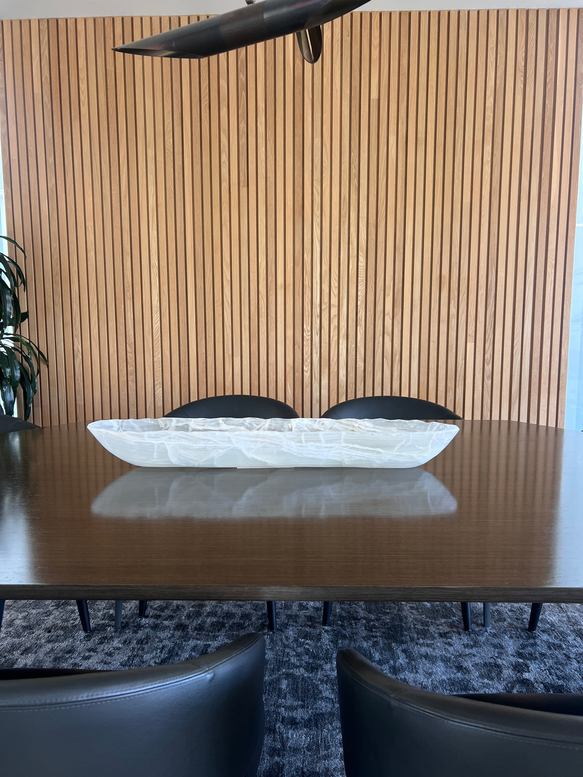 Dining table with a centerpiece white onyx bowl and chairs against a wooden paneled wall.