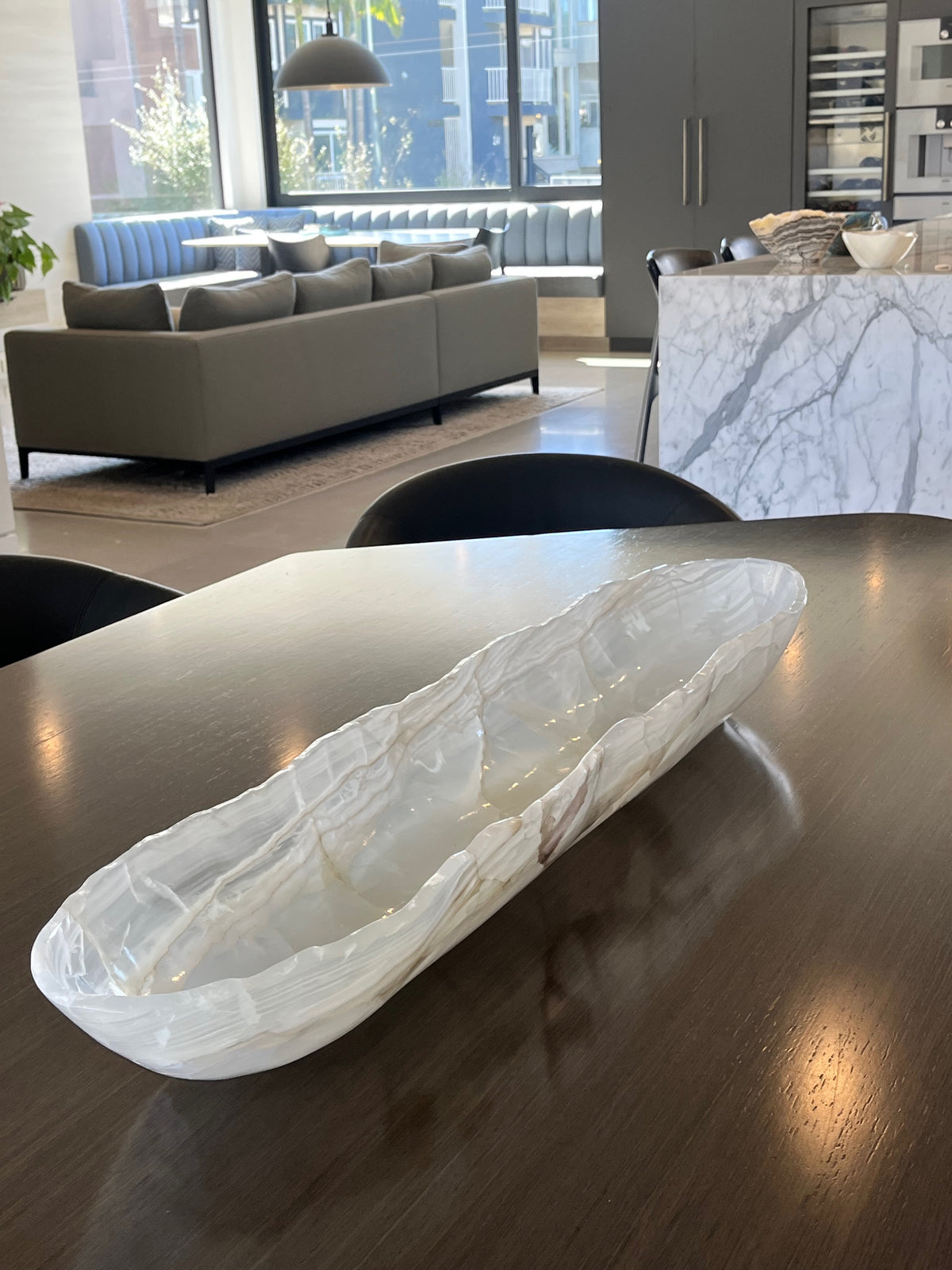 White onyx oblong bowl on a wooden table with a modern living room in the background