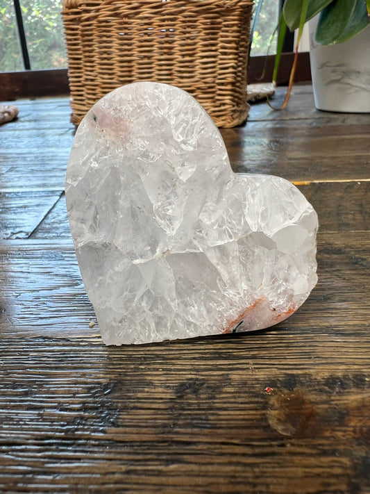 Heart-shaped crystal on a wooden surface with a wicker basket and plant in the background