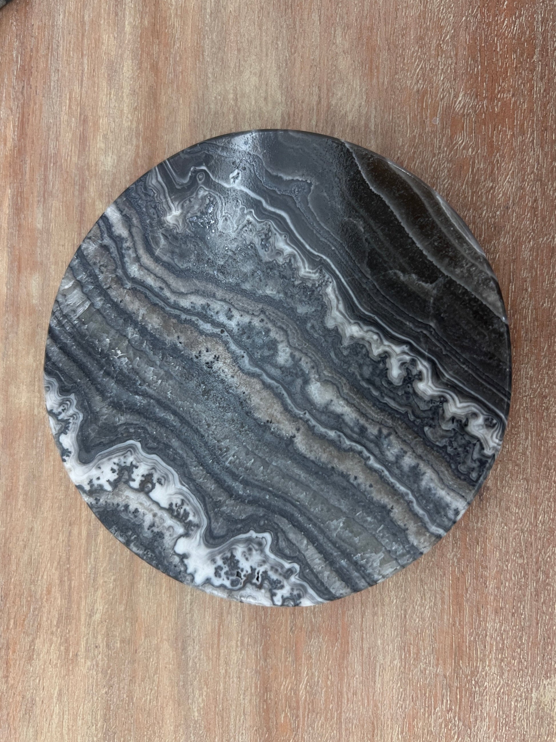 Round black banded calcite coaster with gray and white patterns on a wooden surface