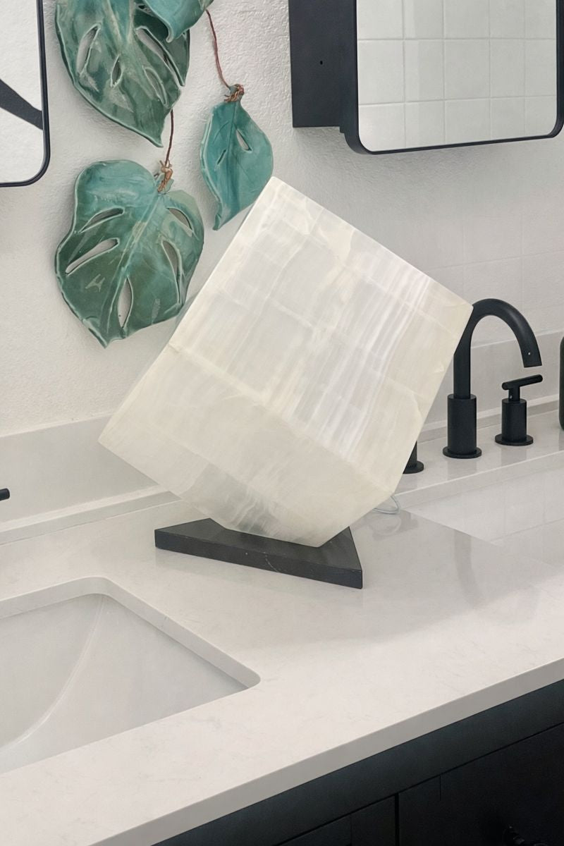 White onyx cube lamp unlit on bathroom vanity, sculptural stone decor with natural veining, 10 inch cube accent lighting