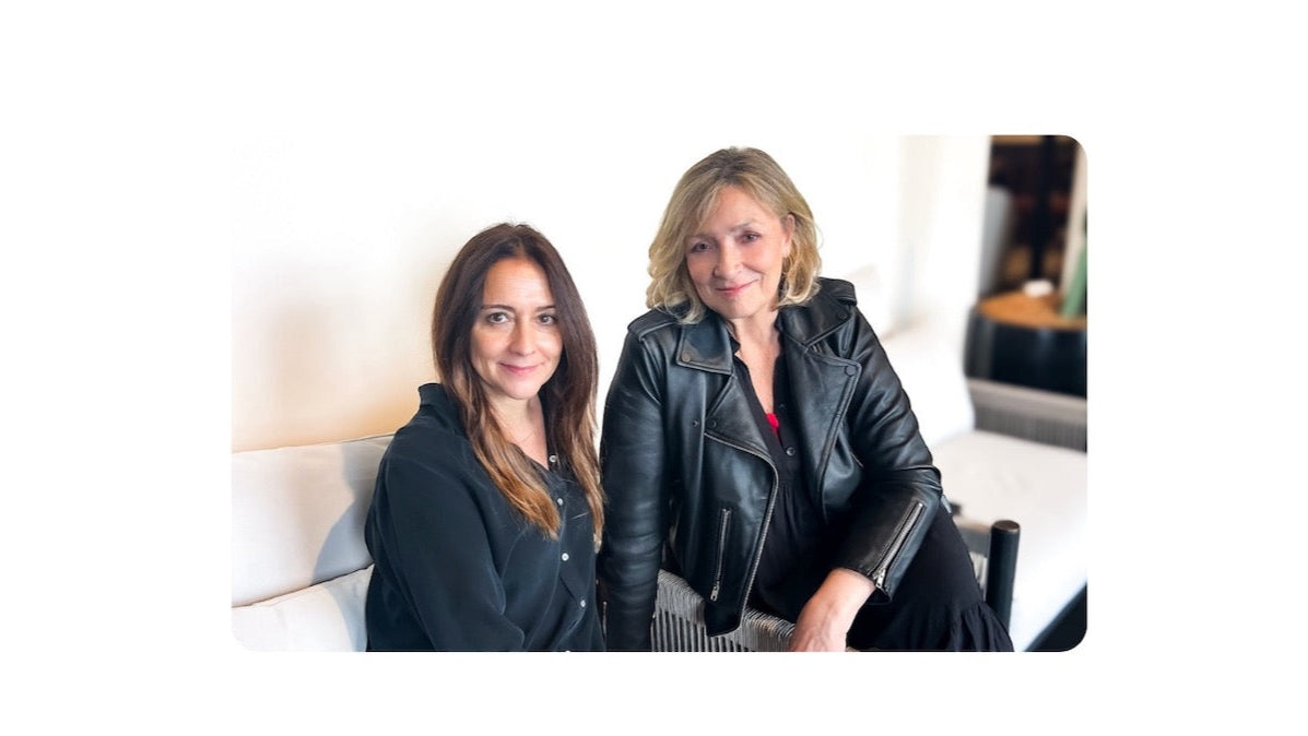 Two women sitting on a couch in a room with a mirror in the background