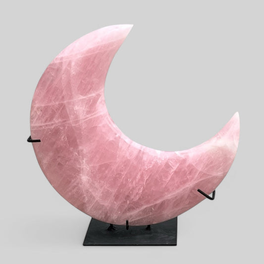A polished, pink rose quartz crystal in a crescent shape, mounted on a black stand.