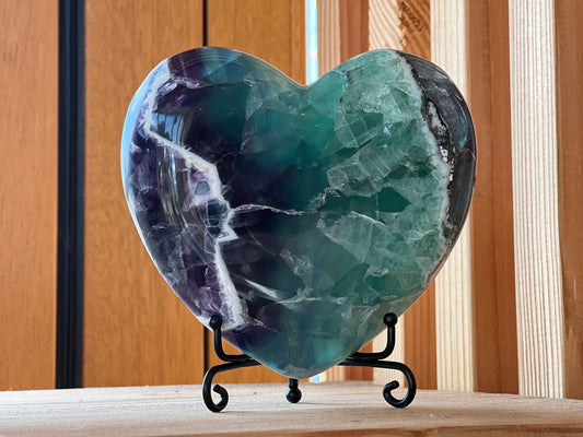 A polished heart-shaped fluorite crystal displayed on a stand, with a rich display of green and purple hues.