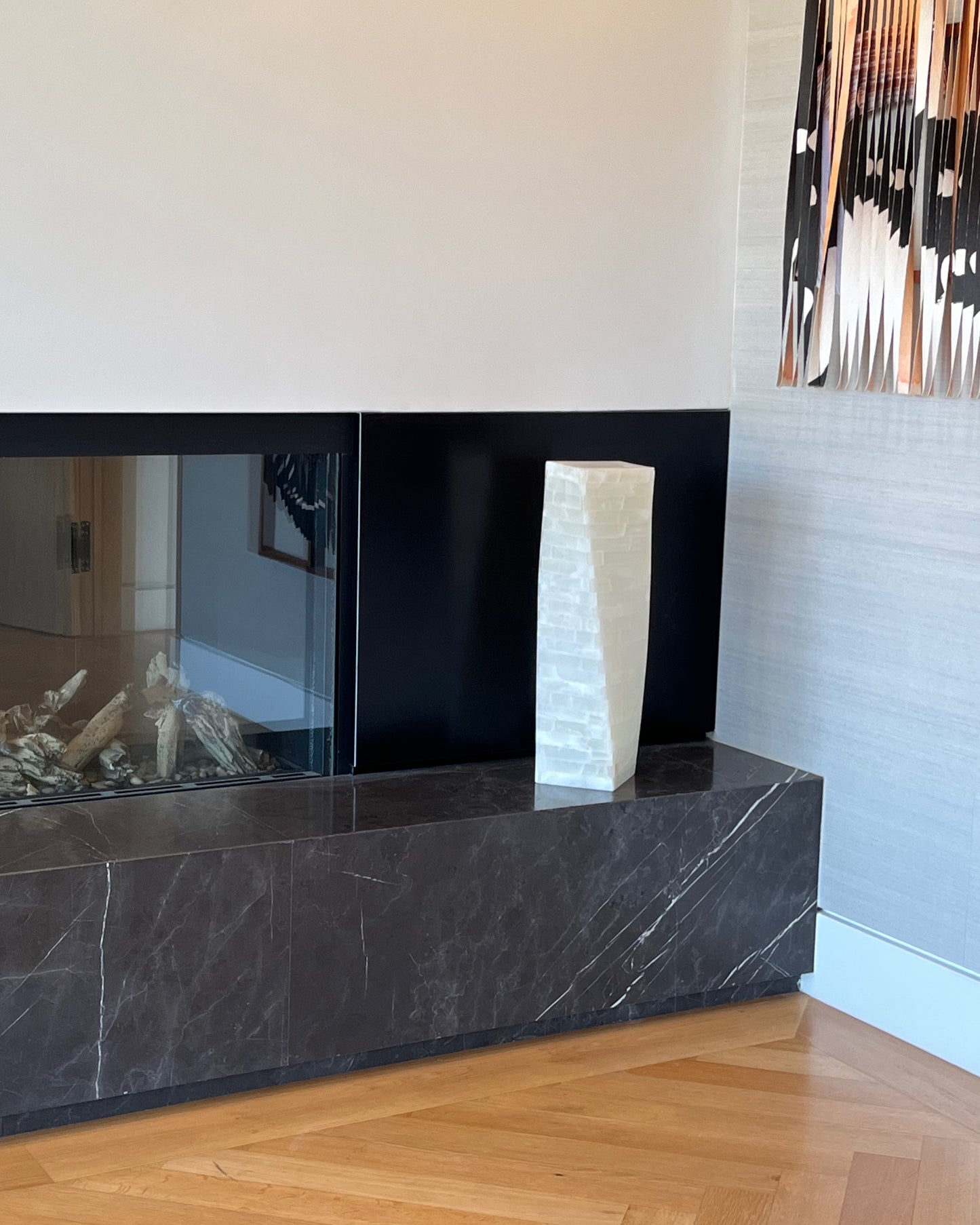 Modern fireplace with black marble surround and white vase on a wooden floor.