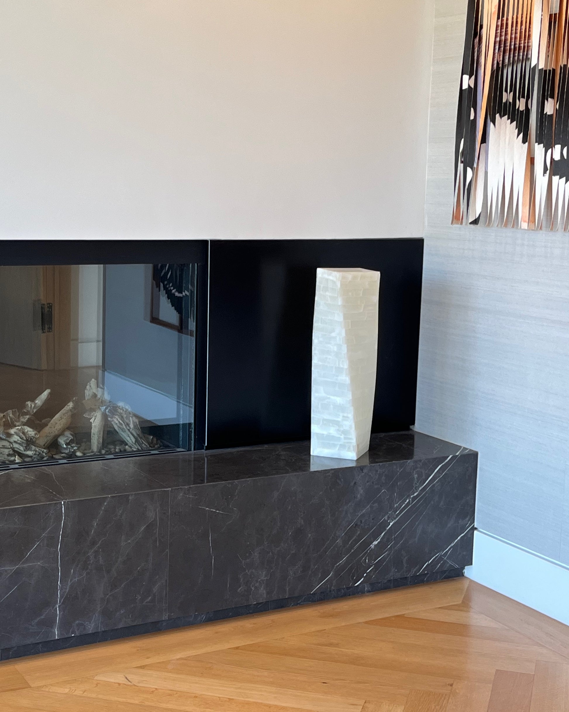 Modern fireplace with black marble surround and white vase on a wooden floor.