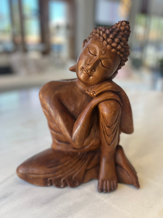 Brown wooden Buddha on a white surface with blurred background