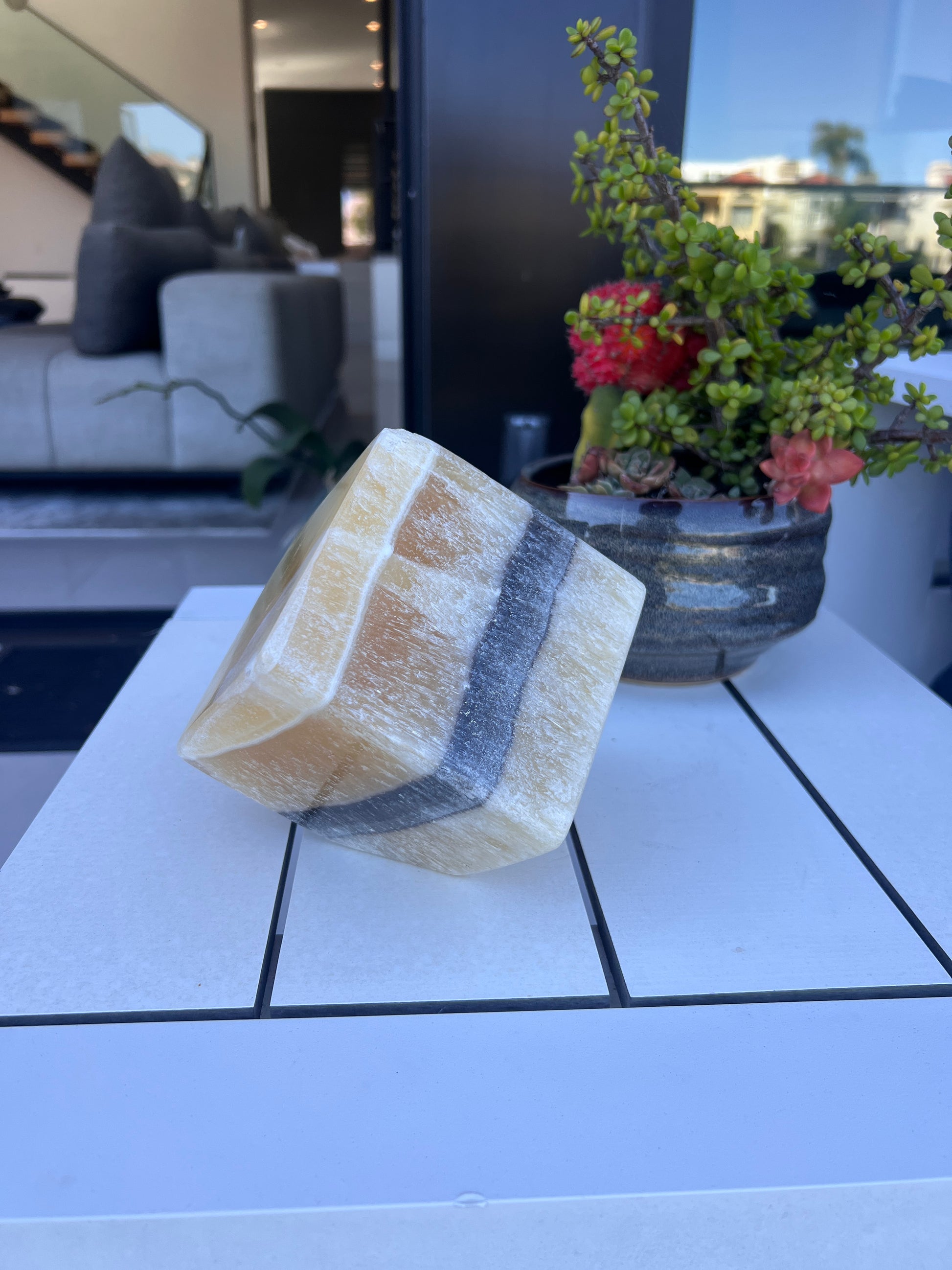 Decorative stone cube with yellow and black bands on a white surface with a blurred indoor background