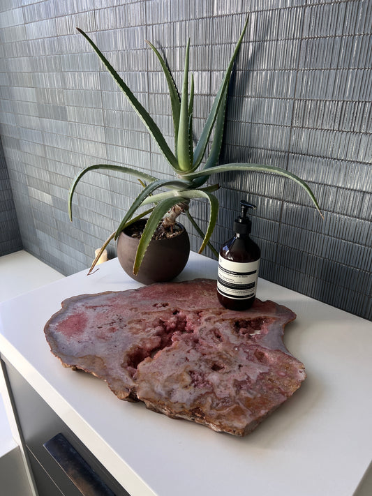 Potted aloe vera plant and bottles on a pink amethyst slab surface with tiled wall background