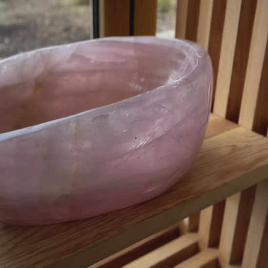 close up video of large dark pink rose quartz bowl on wood shelf near window