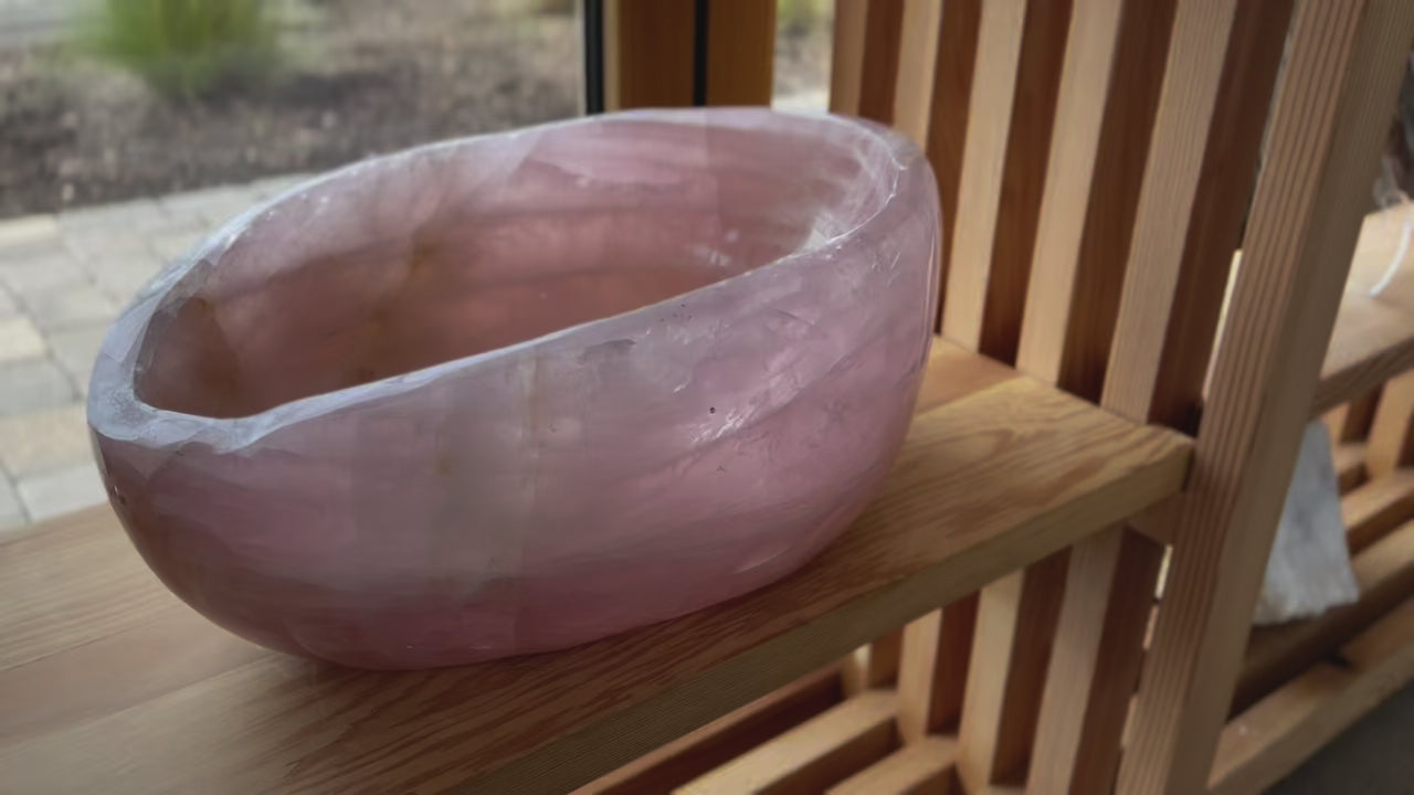 close up video of large dark pink rose quartz bowl on wood shelf near window
