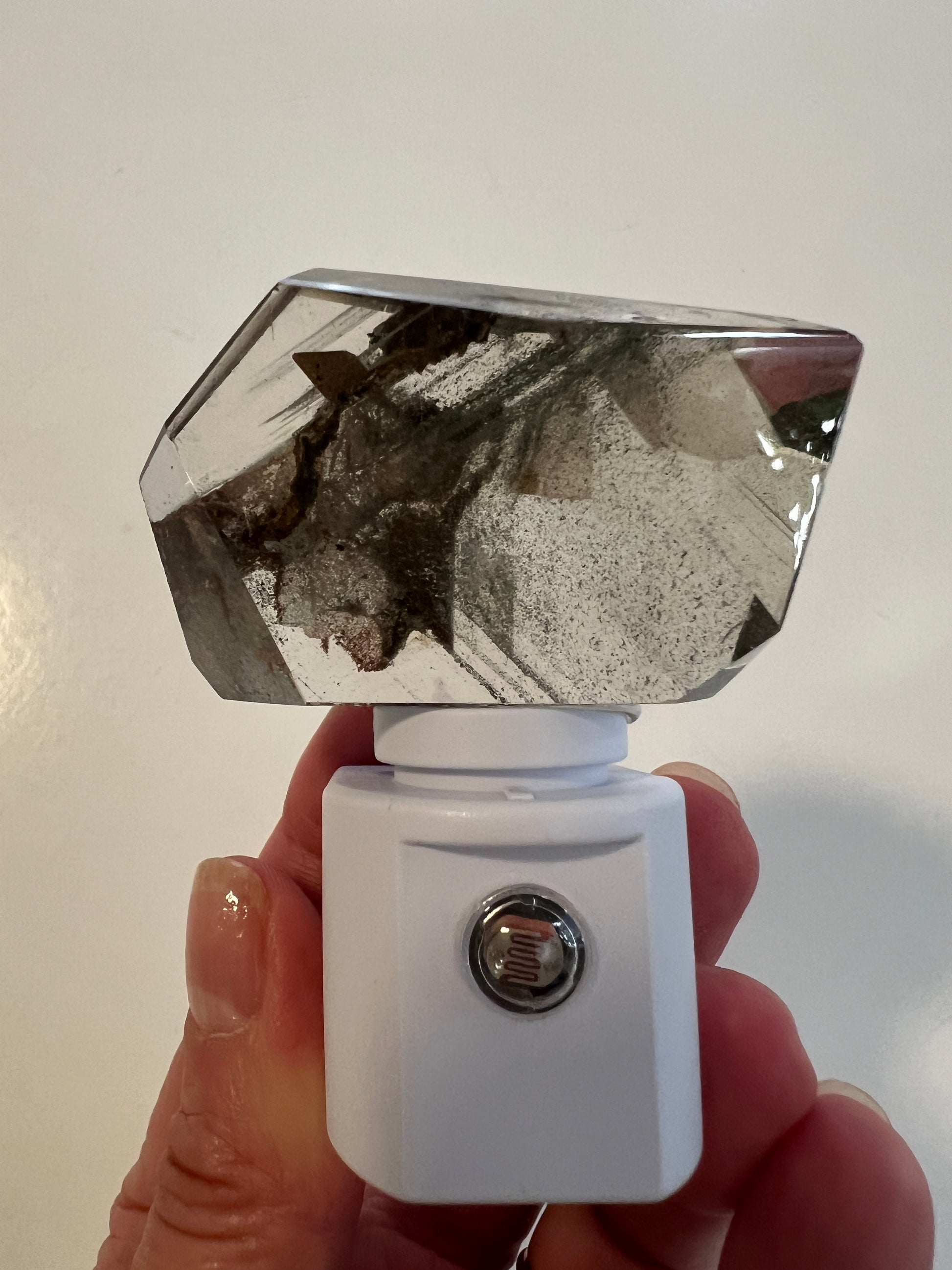 Hand holding a small white night light with a clear phantom quartz on a light background